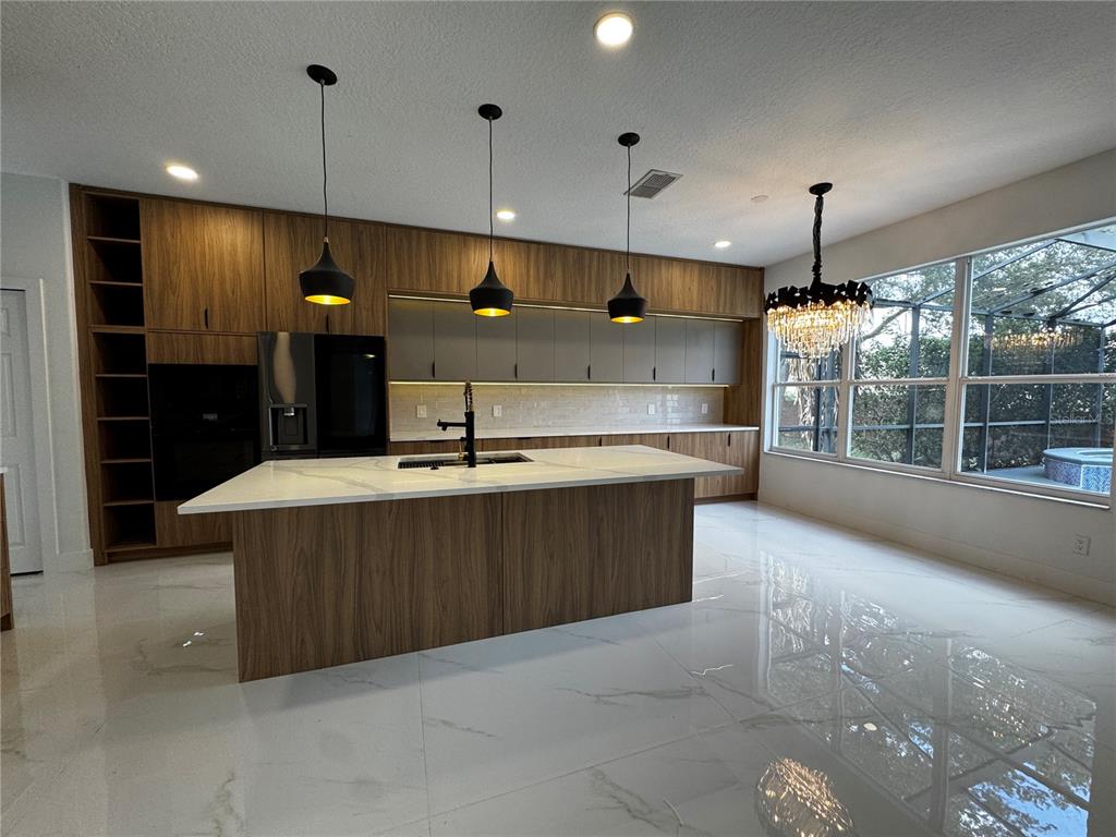 A modern kitchen features wood-grain cabinetry, a white marble island, and black pendant lighting — 219 LARGOVISTA DRIVE, OAKLAND, FL