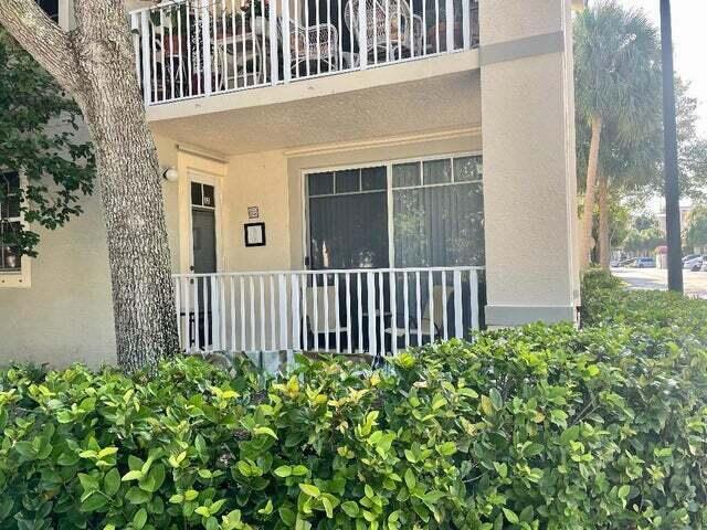 A ground-floor apartment patio features a white railing, sliding glass doors, and a side door — 4736 Chancellor Drive # 13, Jupiter FL 33458, JUPITER, FL