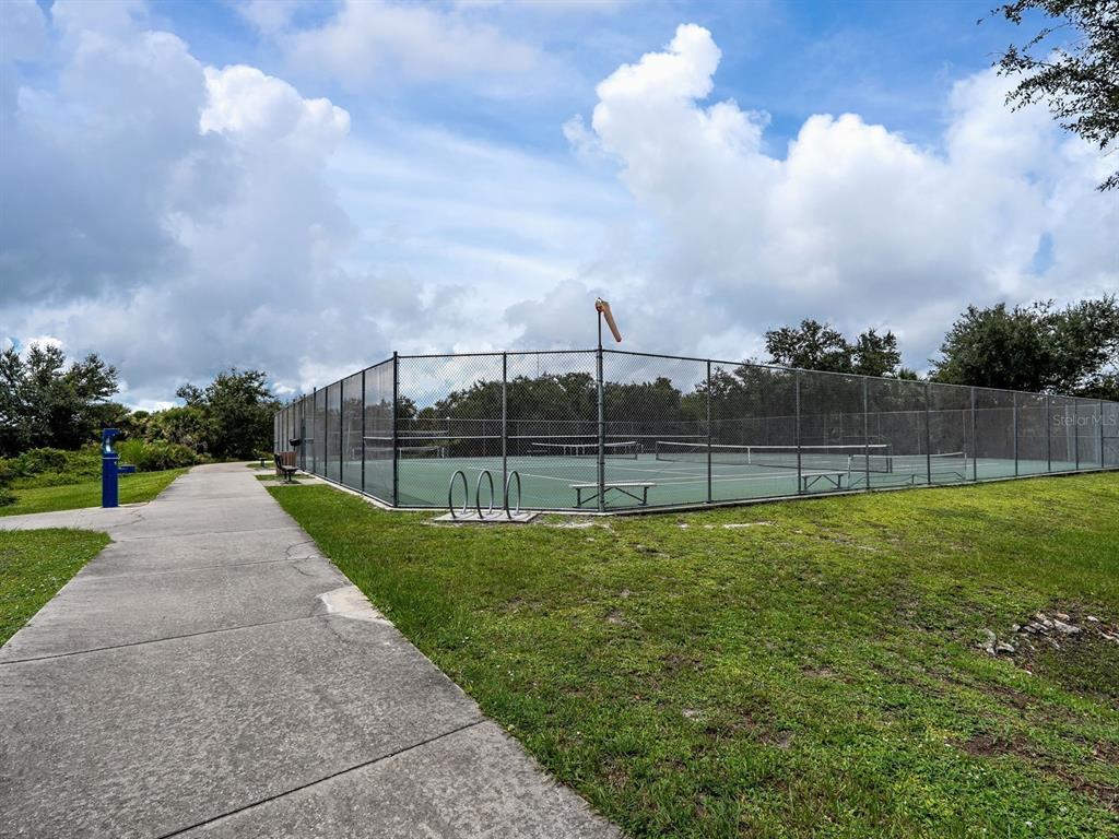 A fenced tennis court sits next to a concrete walkway and a grassy area — 104 ARROW LANE, ROTONDA WEST, FL