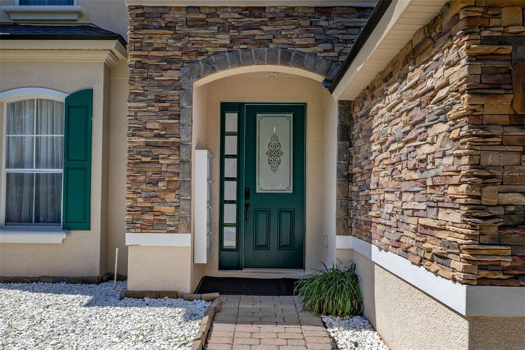 A green front door with a glass insert sits under a stone-accented arched entryway — 13247 HATHERTON CIRCLE, ORLANDO, FL