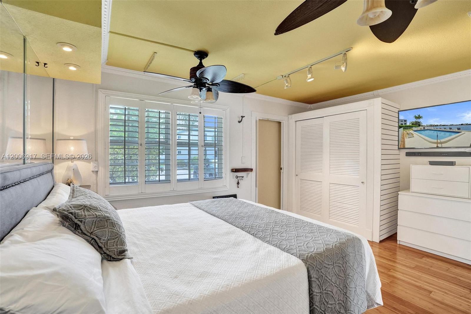 A bedroom features a yellow ceiling, a ceiling fan, white louvered closet doors, and shutters — 1105 S Riverside Dr # 107, Pompano Beach FL 33062, POMPANO BEACH, FL