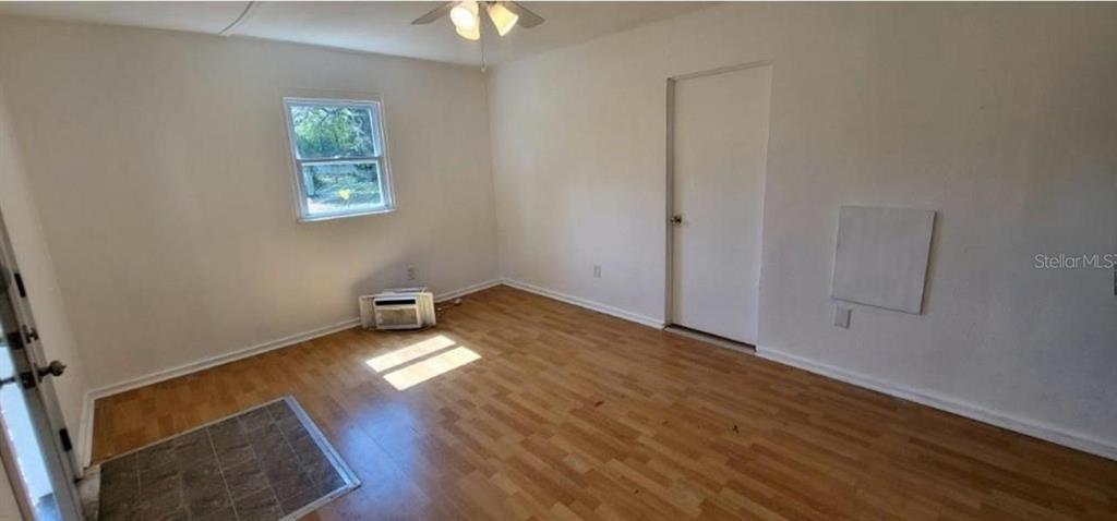 An empty room features light wood-look flooring, a window, a white door, and a ceiling light — 912 ENGMAN STREET, CLEARWATER, FL