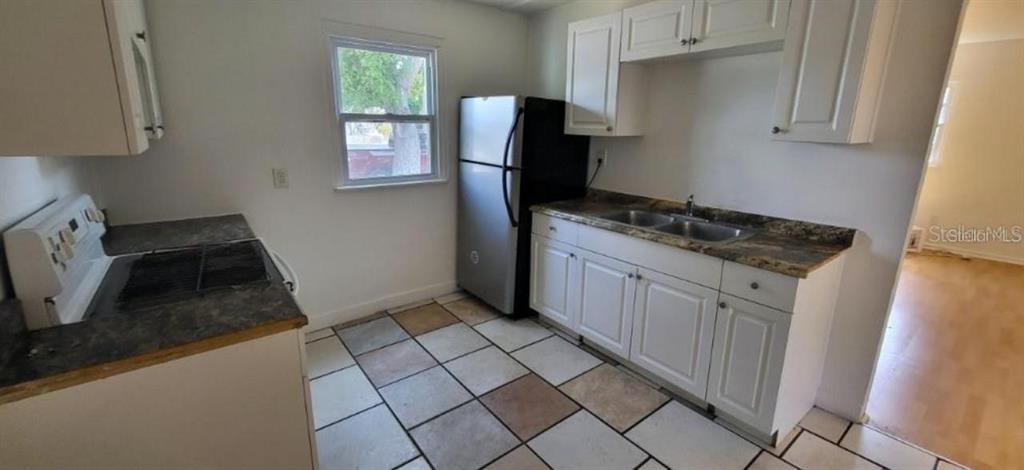 A kitchen features white cabinets, a stainless steel refrigerator, a stove, and tiled flooring — 912 ENGMAN STREET, CLEARWATER, FL