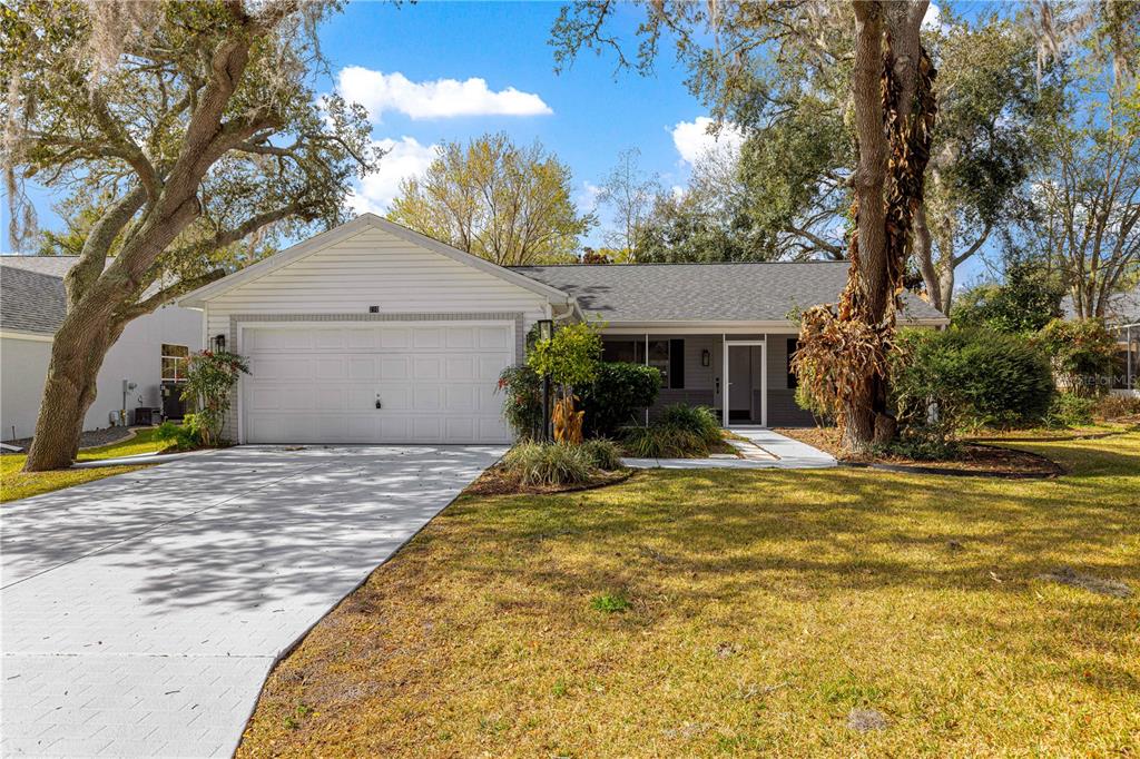 A single-story house with a white garage door, gray roof, and large trees in front — 210 PALERMO PLACE, LADY LAKE, FL