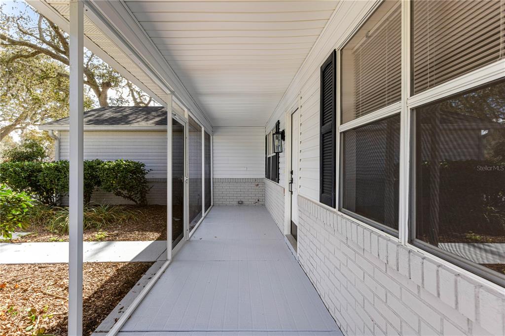A covered porch with a painted brick base, white siding, and a screened-in enclosure — 210 PALERMO PLACE, LADY LAKE, FL