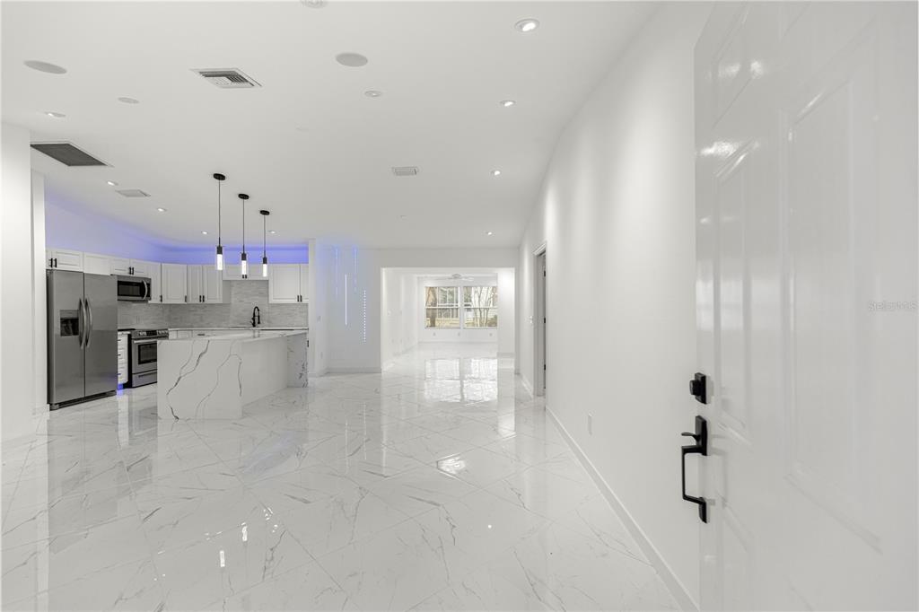 A modern, open-concept kitchen and living area features white marble flooring and white cabinetry — 210 PALERMO PLACE, LADY LAKE, FL