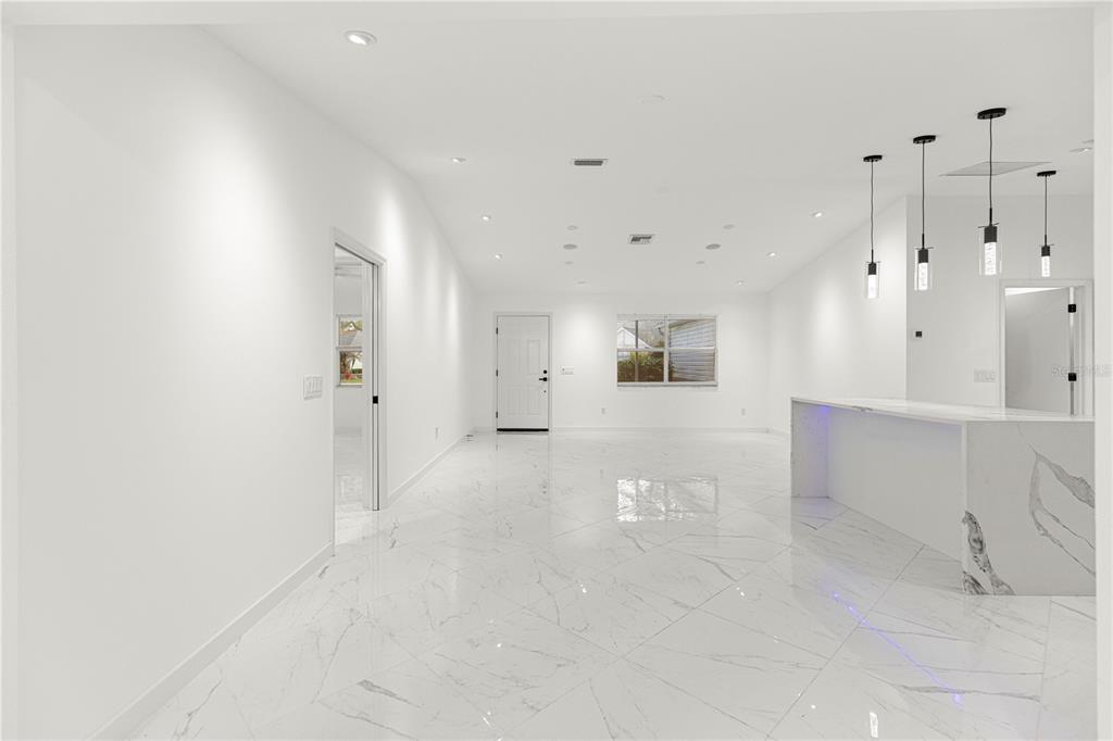 An open-concept living area features white marble-look tile flooring, a kitchen island, and recessed lighting — 210 PALERMO PLACE, LADY LAKE, FL