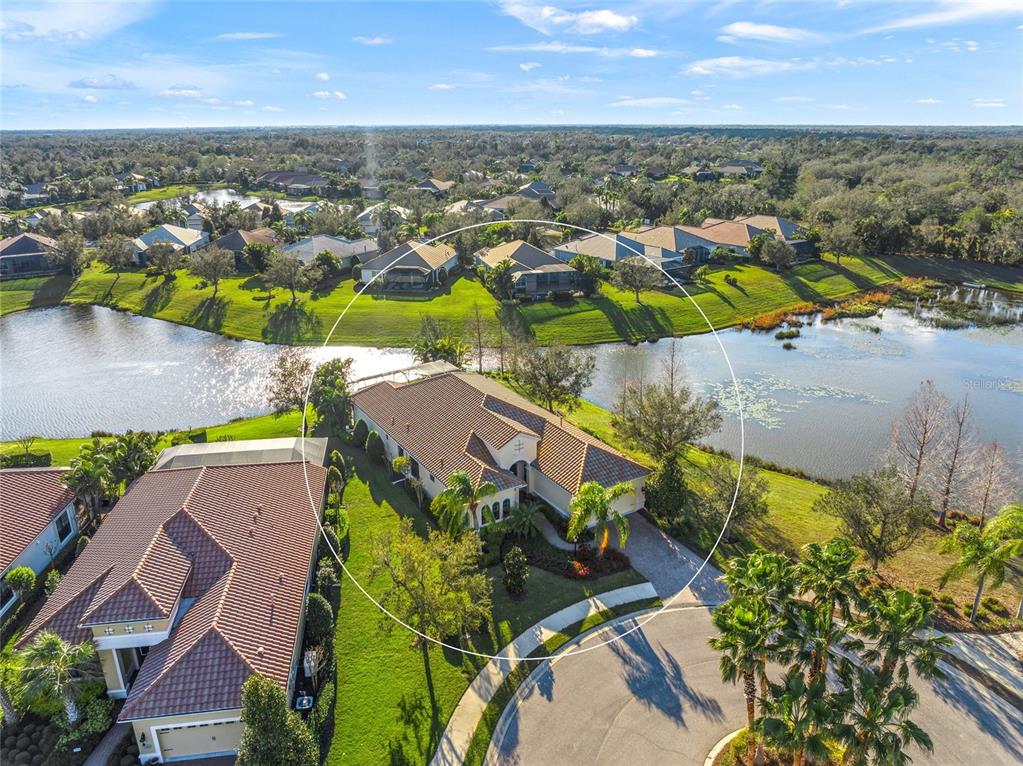 An aerial view shows a single-story house with a tile roof situated on a lakefront lot — 7108 CALLANDER COVE, LAKEWOOD RANCH, FL