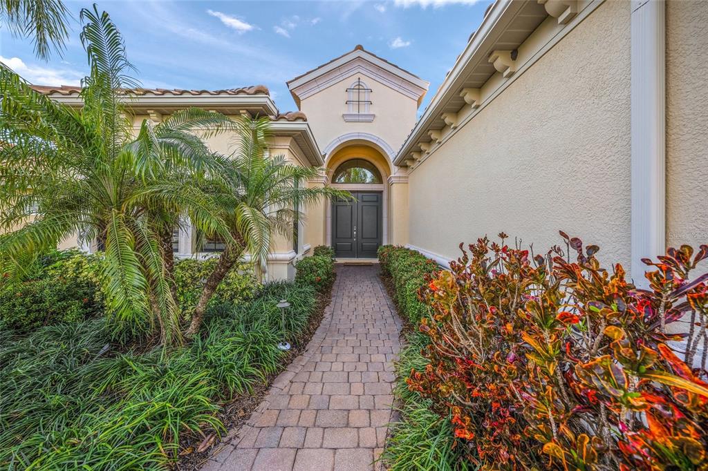 A paved walkway leads to the dark double front doors of a stucco house — 7108 CALLANDER COVE, LAKEWOOD RANCH, FL