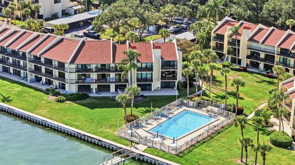 An aerial view shows multi-story apartment buildings with red roofs next to a swimming pool — 7520 SUNSHINE SKYWAY LANE S UNIT T19, ST PETERSBURG, FL