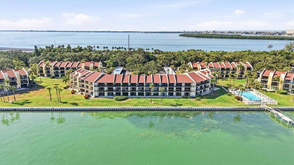 An aerial view shows a multi-story waterfront apartment complex with a pool and green lawn — 7520 SUNSHINE SKYWAY LANE S UNIT T19, ST PETERSBURG, FL