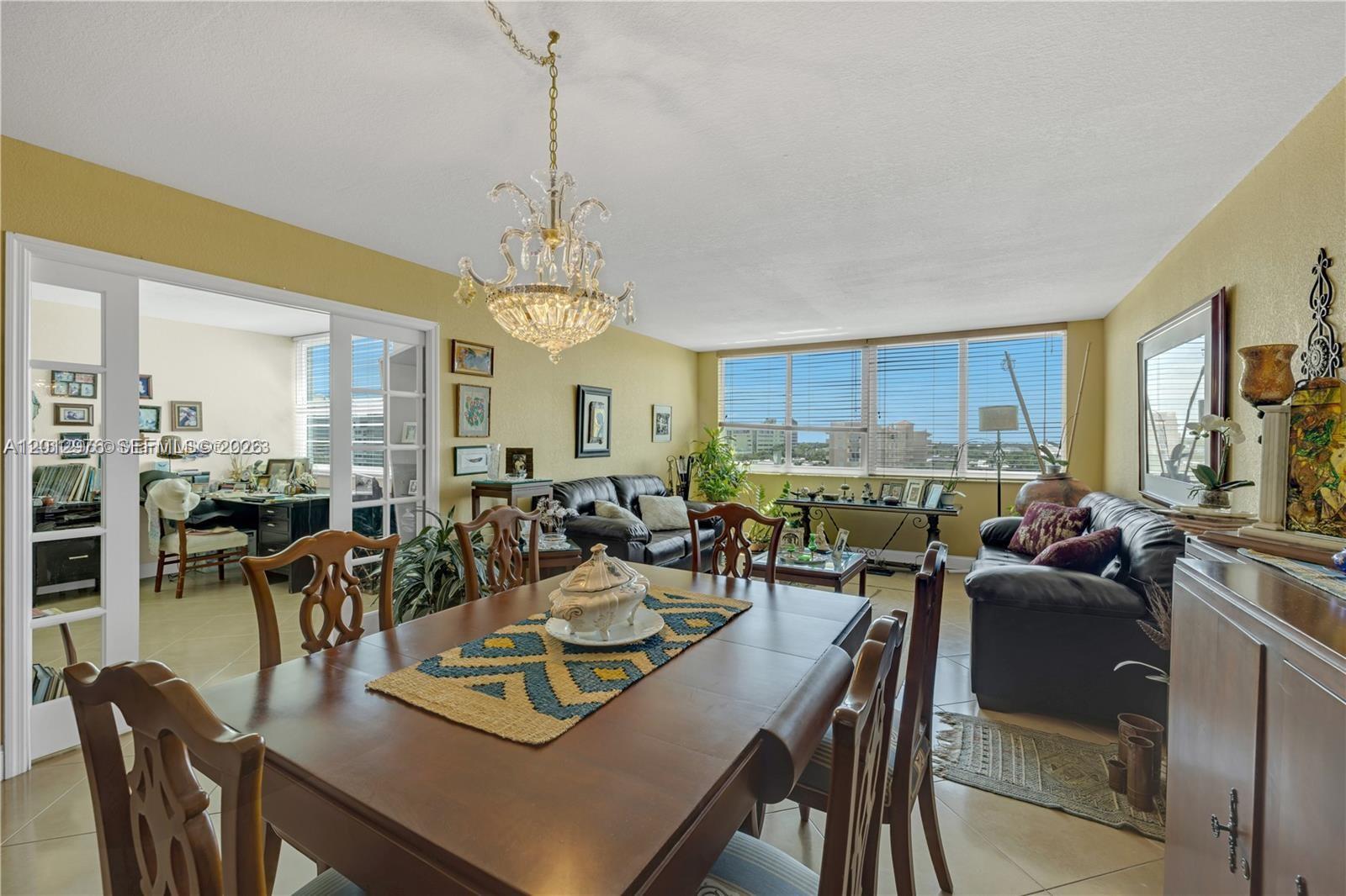A dining area with a chandelier and wooden table opens into a living room with windows — 9125 SW 77th Ave # 802, Miami FL 33156, MIAMI, FL