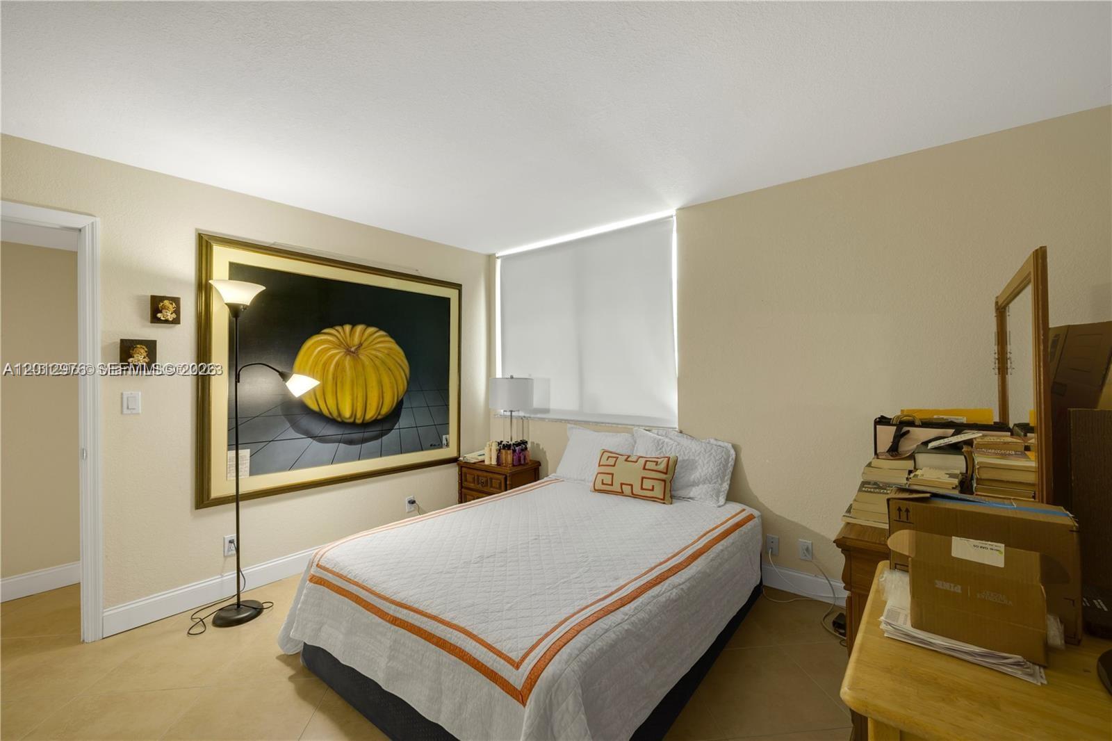 A bedroom features a bed with an orange-trimmed quilt, a large pumpkin painting, and tile flooring — 9125 SW 77th Ave # 802, Miami FL 33156, MIAMI, FL