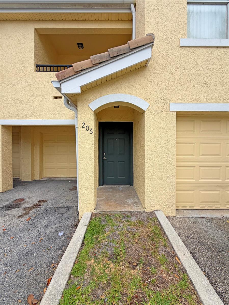 The exterior of a yellow stucco townhouse features a dark green front door labeled 206 — 124 SW Peacock Boulevard # 206, FL 34986, FL