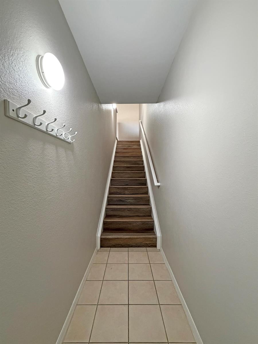 A staircase with wood-look treads leads upward from a tiled entryway with wall hooks — 124 SW Peacock Boulevard # 206, FL 34986, FL