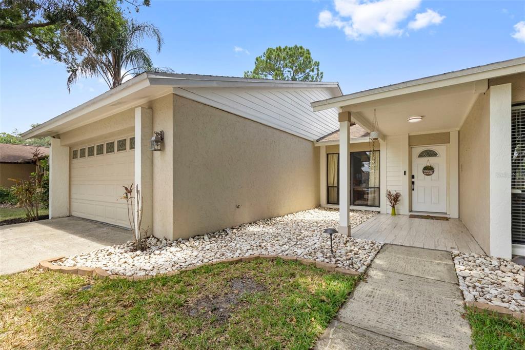 A beige house exterior features a garage, a covered entryway, and a rock-covered front yard — 15701 COUNTRY LAKE DRIVE, TAMPA, FL
