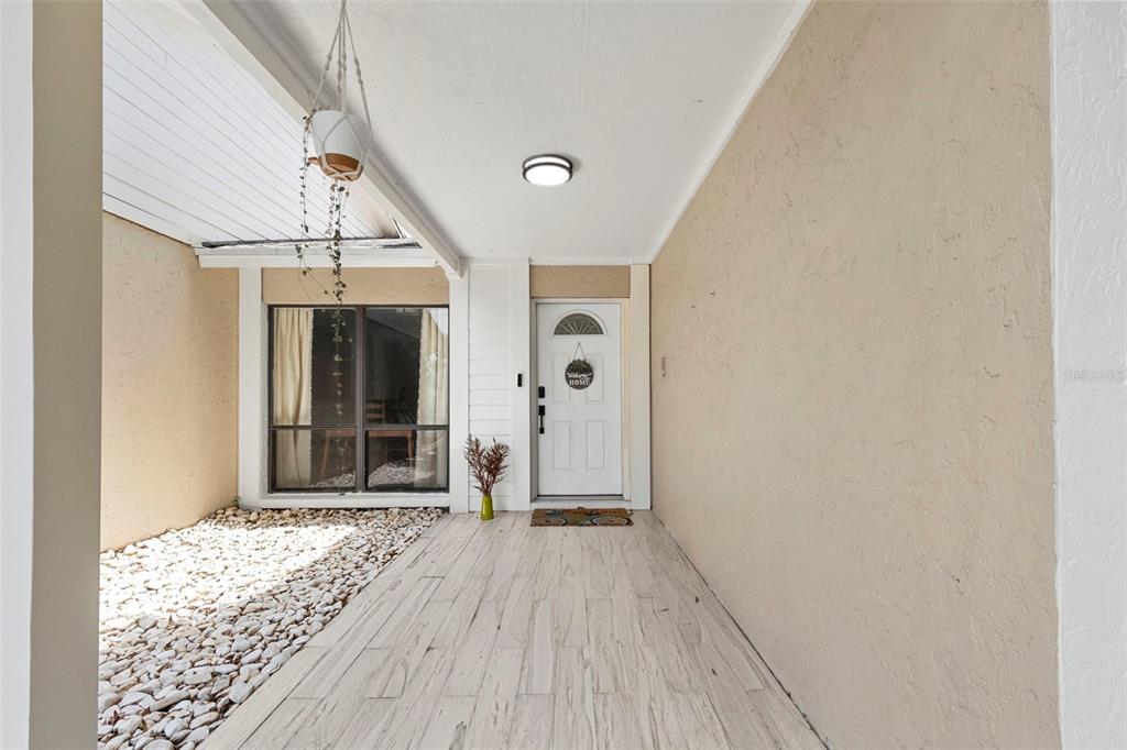 A covered entryway features light-colored wood-look tile flooring, a white front door, and a window — 15701 COUNTRY LAKE DRIVE, TAMPA, FL