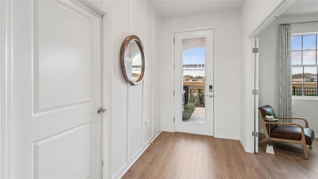 An entryway features white board-and-batten walls, wood-look flooring, a round mirror, and a glass-paneled door — 5434 SW 55TH TERRACE, GAINESVILLE, FL