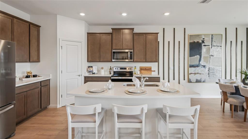 A kitchen with brown cabinets, a white island, stainless steel appliances, and light wood flooring — 5434 SW 55TH TERRACE, GAINESVILLE, FL