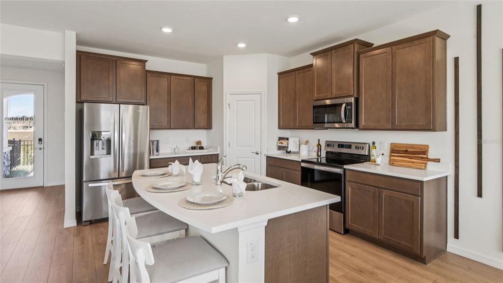 A kitchen features brown cabinets, stainless steel appliances, a white island, and light wood flooring — 5434 SW 55TH TERRACE, GAINESVILLE, FL