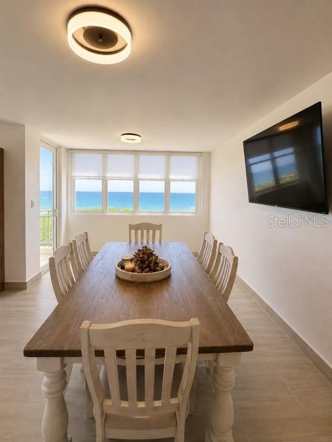 A dining room features a wooden table, white chairs, and a large window overlooking the ocean — 67 AQUAMARINA UNIT Jobos, ISABELA, PR