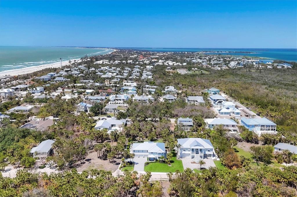An aerial view shows a coastal neighborhood with houses nestled among trees near the beach — 355 BARBAROSA STREET, BOCA GRANDE, FL