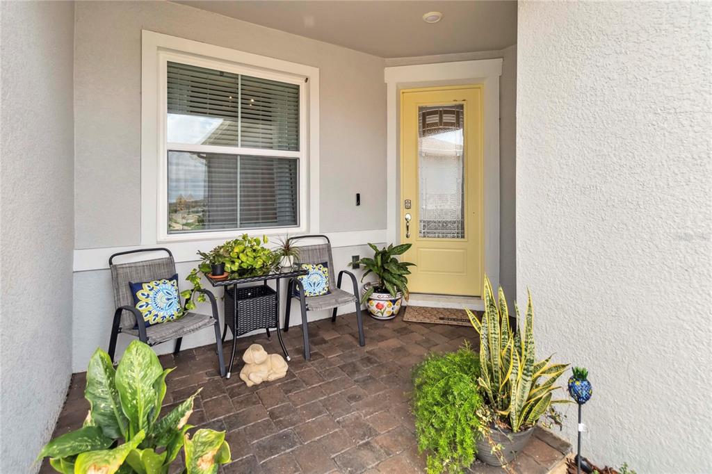 A covered front porch features a yellow door, two chairs, a small table, and potted plants — 1895 SPRING SHOWER CIRCLE, KISSIMMEE, FL