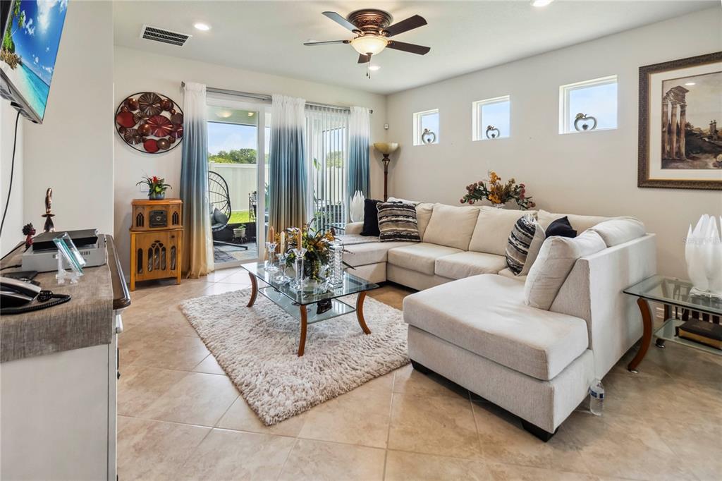 A living room features a large sectional sofa, a glass coffee table, and sliding glass doors — 1895 SPRING SHOWER CIRCLE, KISSIMMEE, FL