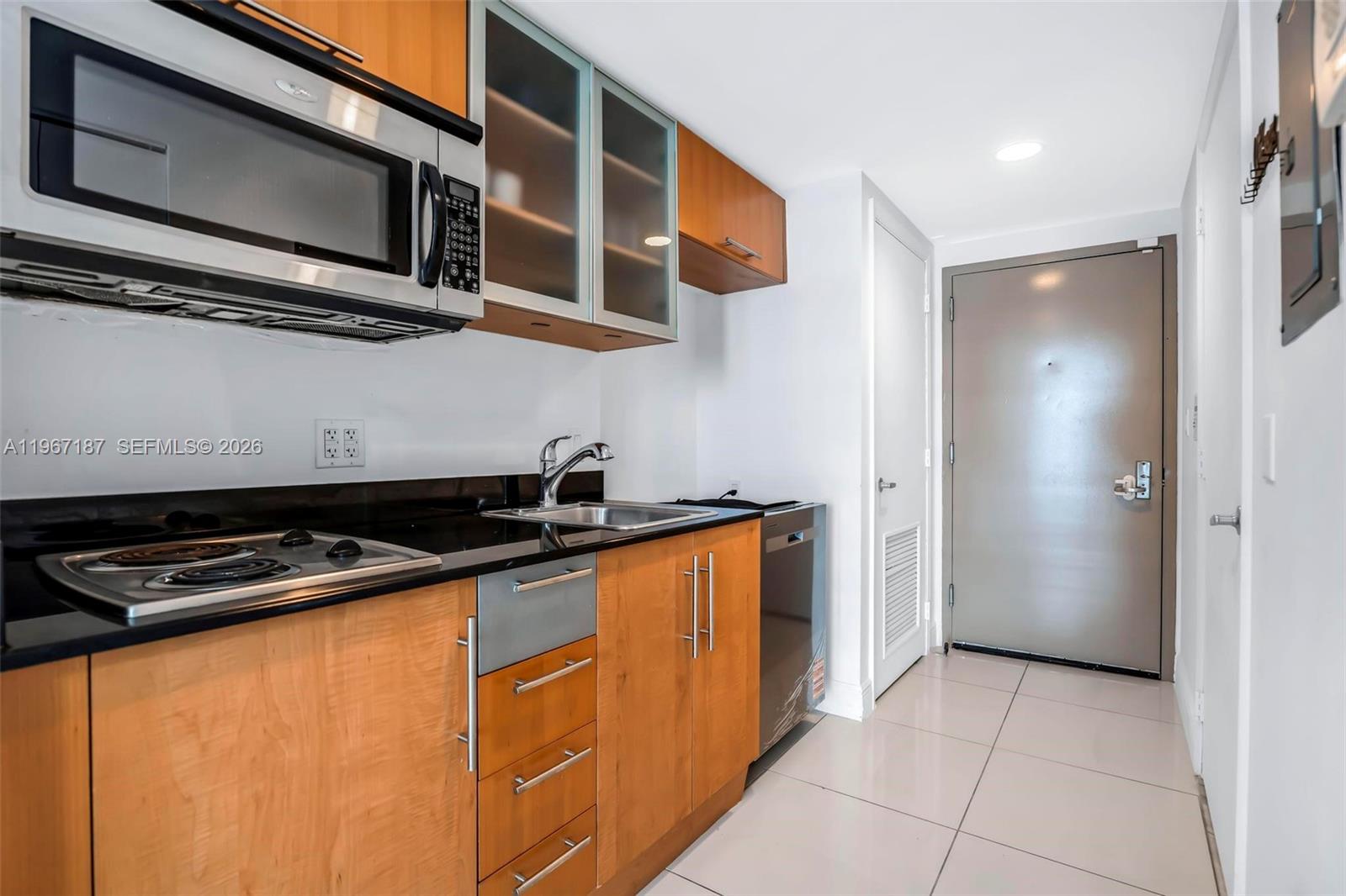 A small kitchen features wood cabinets, black countertops, stainless steel appliances, and tile flooring — 1750 N Bayshore Dr # 4507, Miami FL 33132, MIAMI, FL