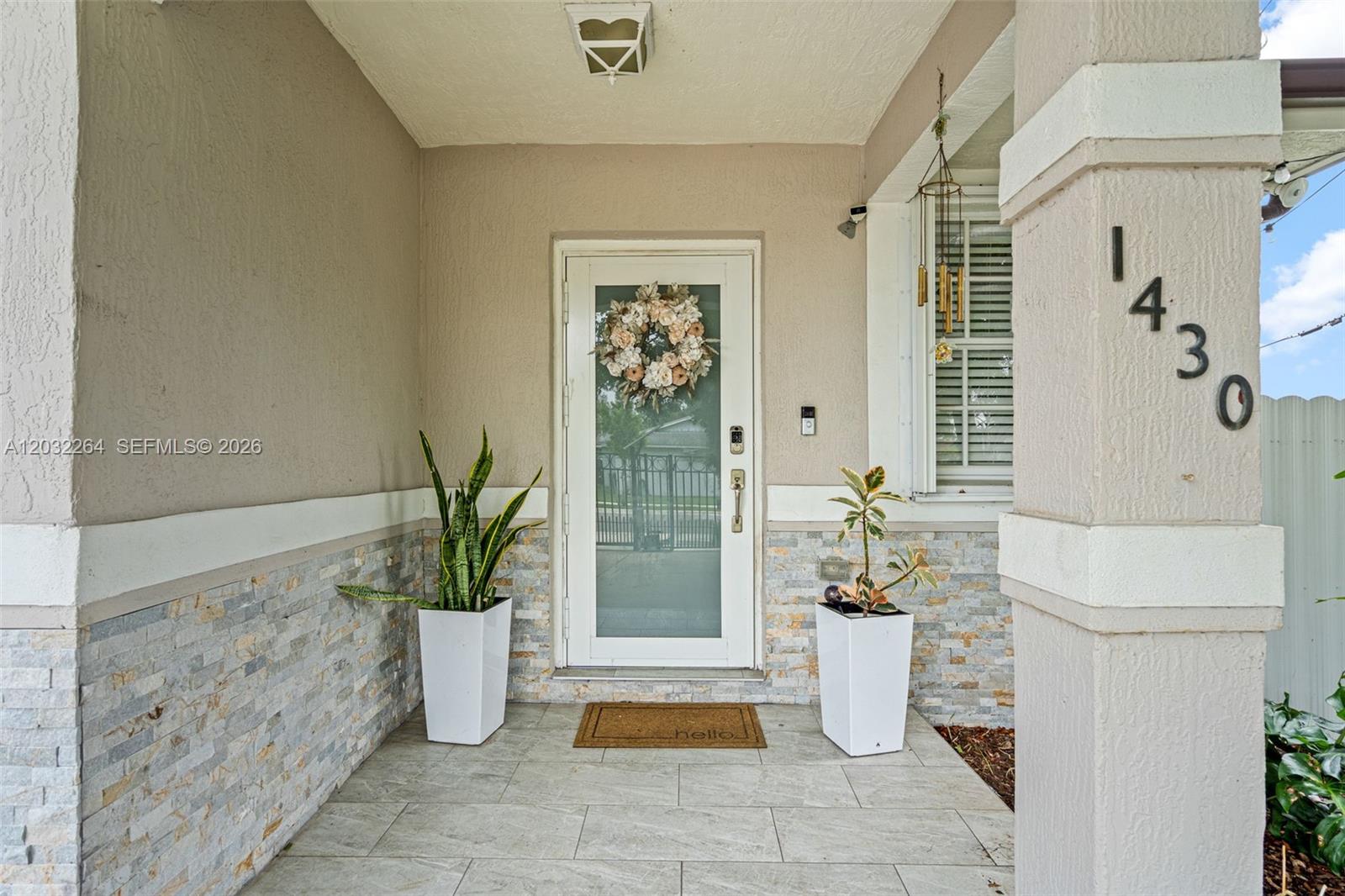 A covered front porch features a glass-paneled door, stone veneer siding, and two potted plants — 1430 NW 5th Ave, Florida City FL 33034, FLORIDA CITY, FL
