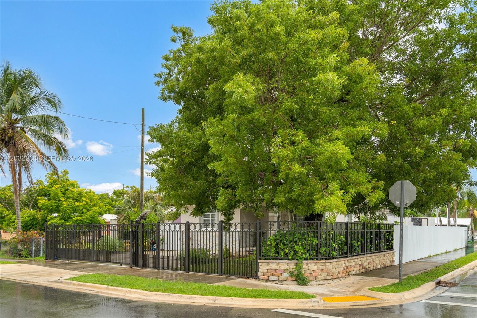 A fenced residential property features a large tree and a stone-based metal gate — 1430 NW 5th Ave, Florida City FL 33034, FLORIDA CITY, FL