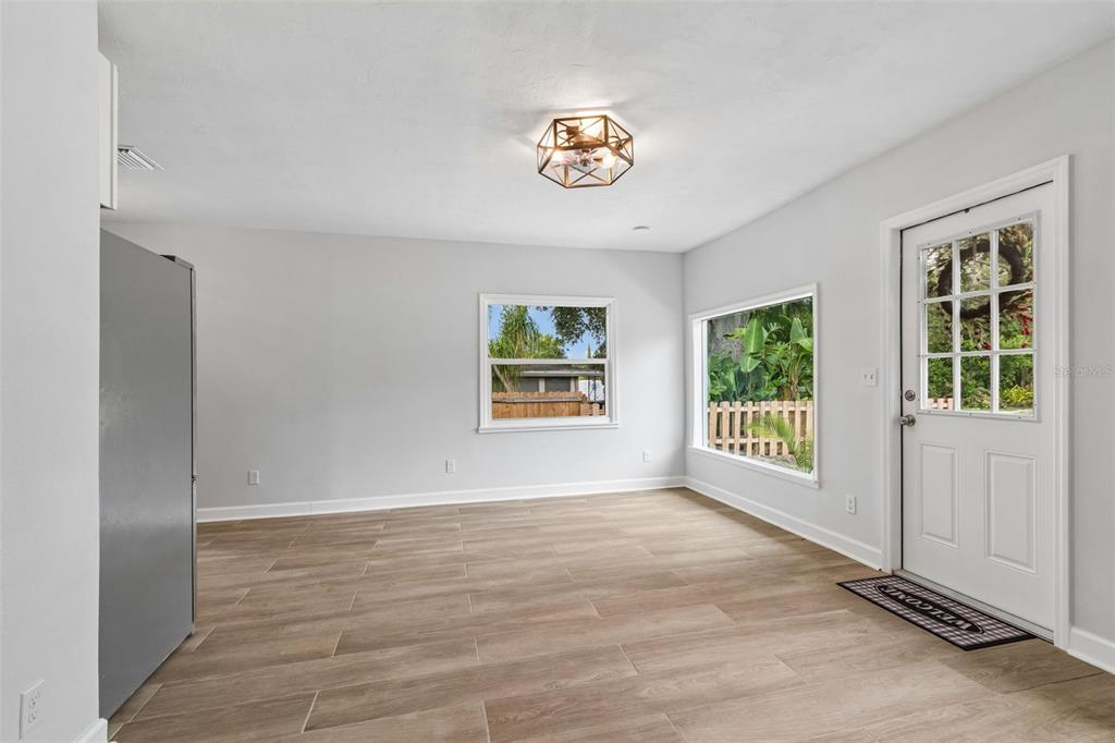 An empty room with light gray walls, wood-look tile flooring, a geometric light fixture, and windows — 1362 MILTON STREET, CLEARWATER, FL