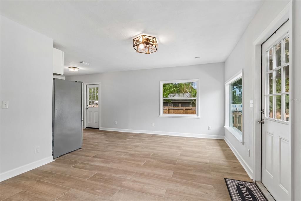 A bright room with light wood-look tile flooring, white walls, a stainless refrigerator, and doors — 1362 MILTON STREET, CLEARWATER, FL