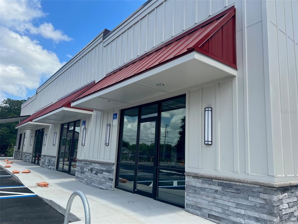 The exterior of a modern commercial building features white vertical siding, stone accents, and red awnings — 24974 SW 4 AVENUE, NEWBERRY, FL