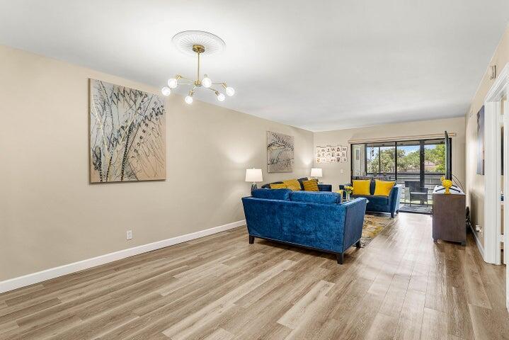 A living room features wood-look flooring, a blue sofa, and a modern chandelier — 10110 Cedar Point Boulevard # 203, Boynton Beach FL 33437, BOYNTON BEACH, FL