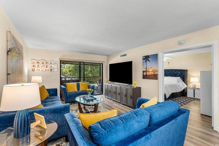 A living room features blue sofas, yellow accent pillows, a television, and an adjacent bedroom — 10110 Cedar Point Boulevard # 203, Boynton Beach FL 33437, BOYNTON BEACH, FL