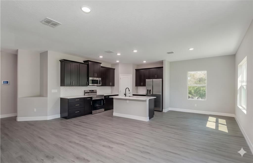 A modern kitchen features dark cabinetry, stainless steel appliances, a center island, and gray flooring — 2039 E NEWHAVEN STREET, INVERNESS, FL