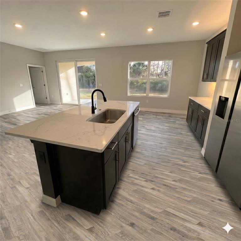 A kitchen features a white quartz island, dark cabinetry, stainless steel appliances, and wood-look flooring — 2039 E NEWHAVEN STREET, INVERNESS, FL