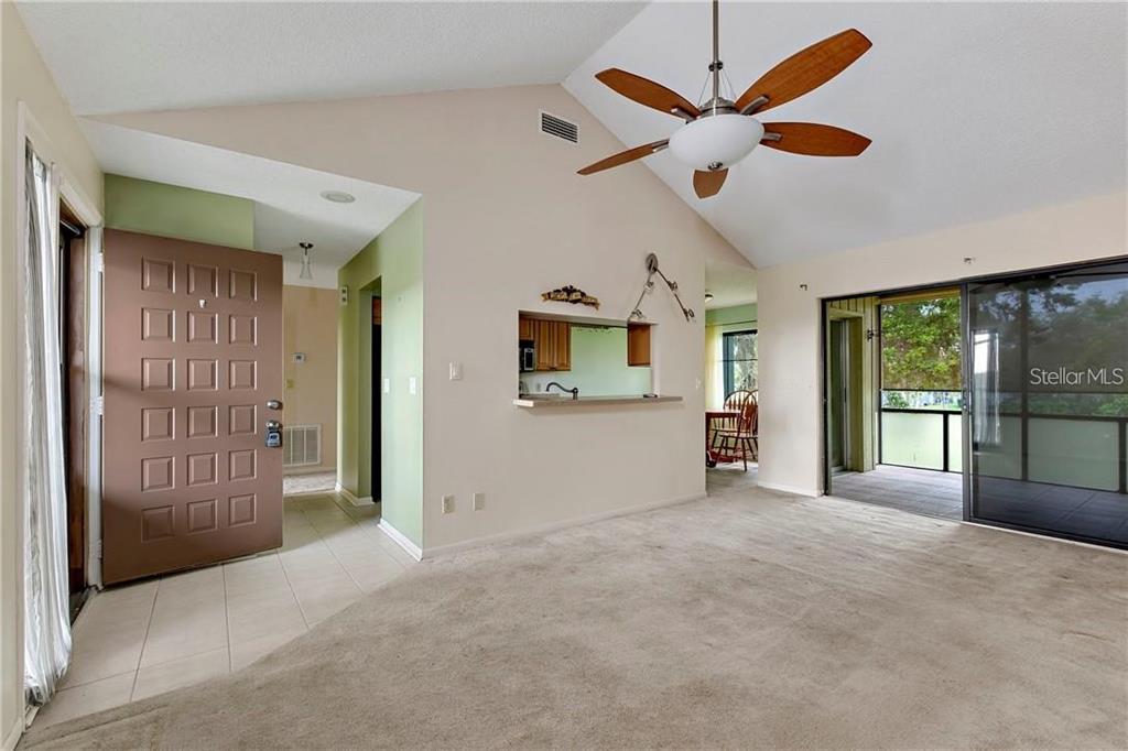 A living room with beige carpet, a vaulted ceiling, a ceiling fan, and a pass-through window — 7 BUCK CIRCLE UNIT 7, HAINES CITY, FL
