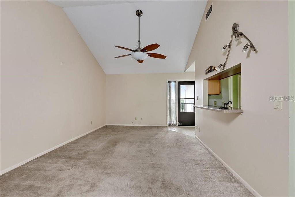 A living room with vaulted ceilings, a ceiling fan, carpeted floors, and a kitchen pass-through — 7 BUCK CIRCLE UNIT 7, HAINES CITY, FL