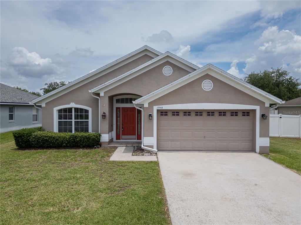 A single-story house with a beige stucco exterior, a red front door, and a garage — 1940 FAWN MEADOW CIRCLE, ST CLOUD, FL
