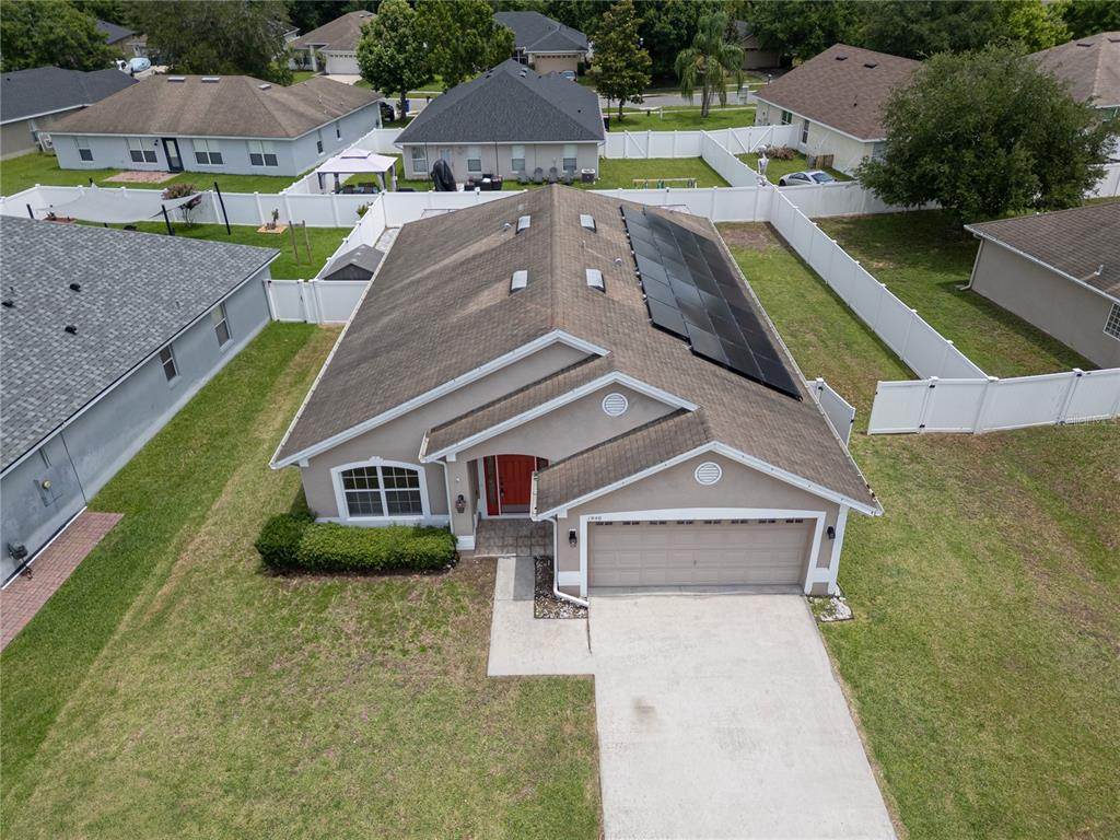 An aerial view shows a single-story house with a tan exterior, red door, and solar panels — 1940 FAWN MEADOW CIRCLE, ST CLOUD, FL