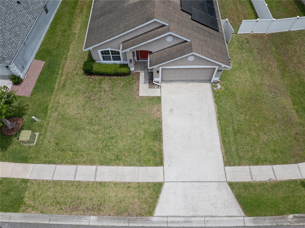 An aerial view shows a single-story house with a concrete driveway and solar panels — 1940 FAWN MEADOW CIRCLE, ST CLOUD, FL
