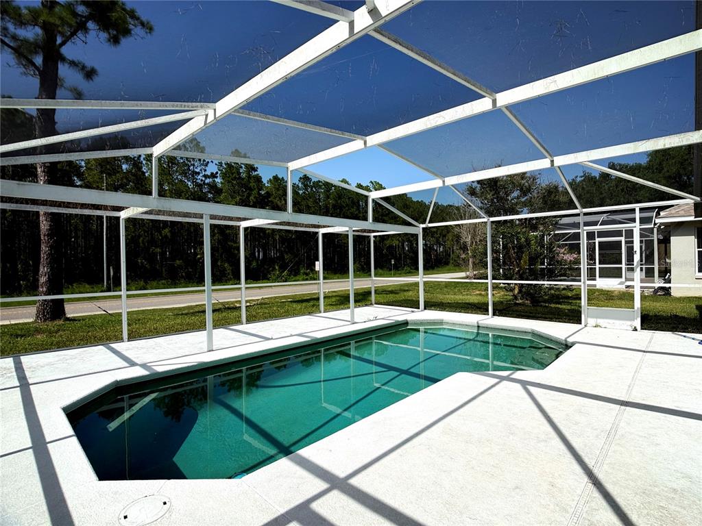 A swimming pool enclosed by a white screen cage sits on a concrete patio — 526 PINE CONE DRIVE, DAVENPORT, FL