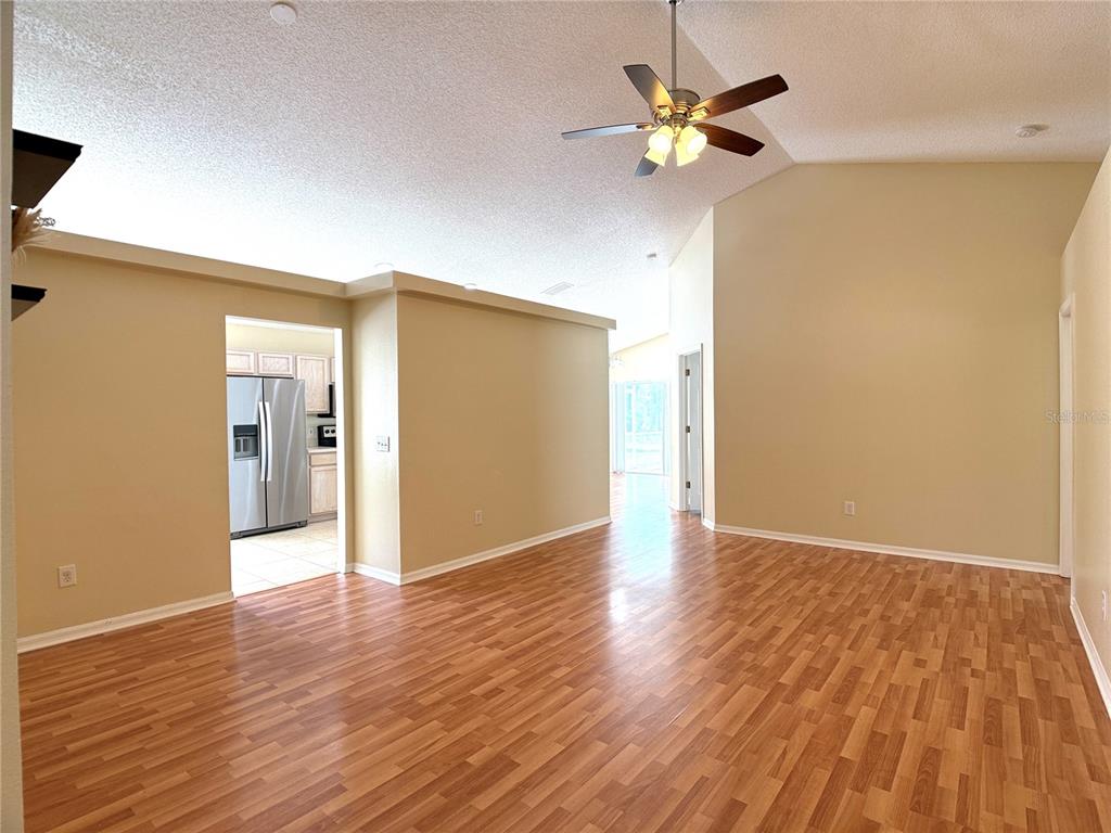 A living room with wood-look laminate flooring, beige walls, and a vaulted ceiling with a fan — 526 PINE CONE DRIVE, DAVENPORT, FL