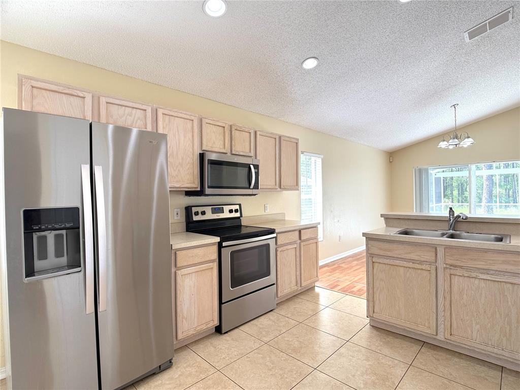 A kitchen with light wood cabinets, stainless steel appliances, and tile flooring — 526 PINE CONE DRIVE, DAVENPORT, FL