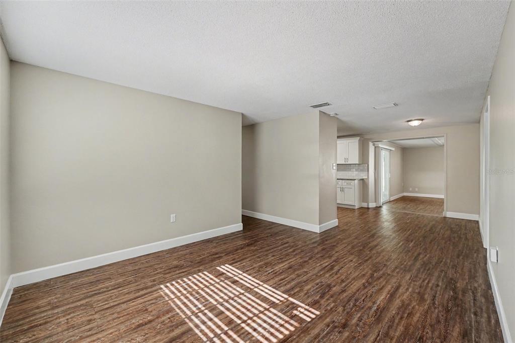 An open-concept living area features wood-look flooring, light-colored walls, and a view into the kitchen — 1615 SENECA AVENUE, LAKELAND, FL