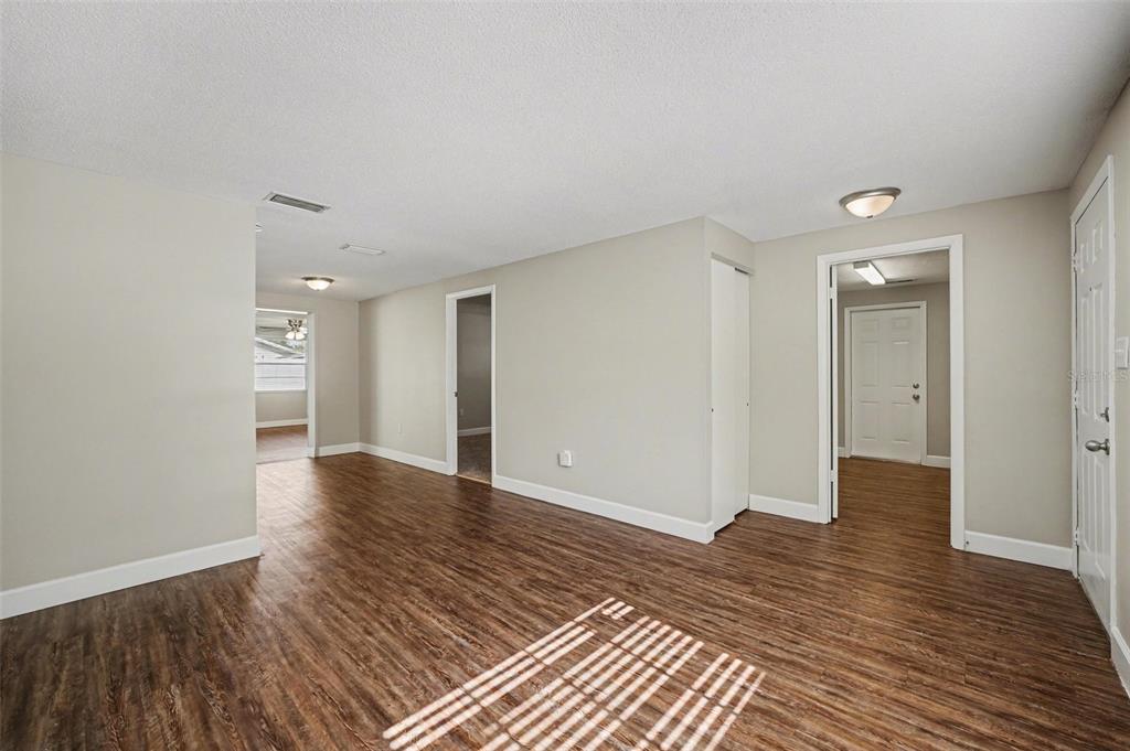 An interior view of a room with wood-look flooring, light-colored walls, and multiple doorways — 1615 SENECA AVENUE, LAKELAND, FL