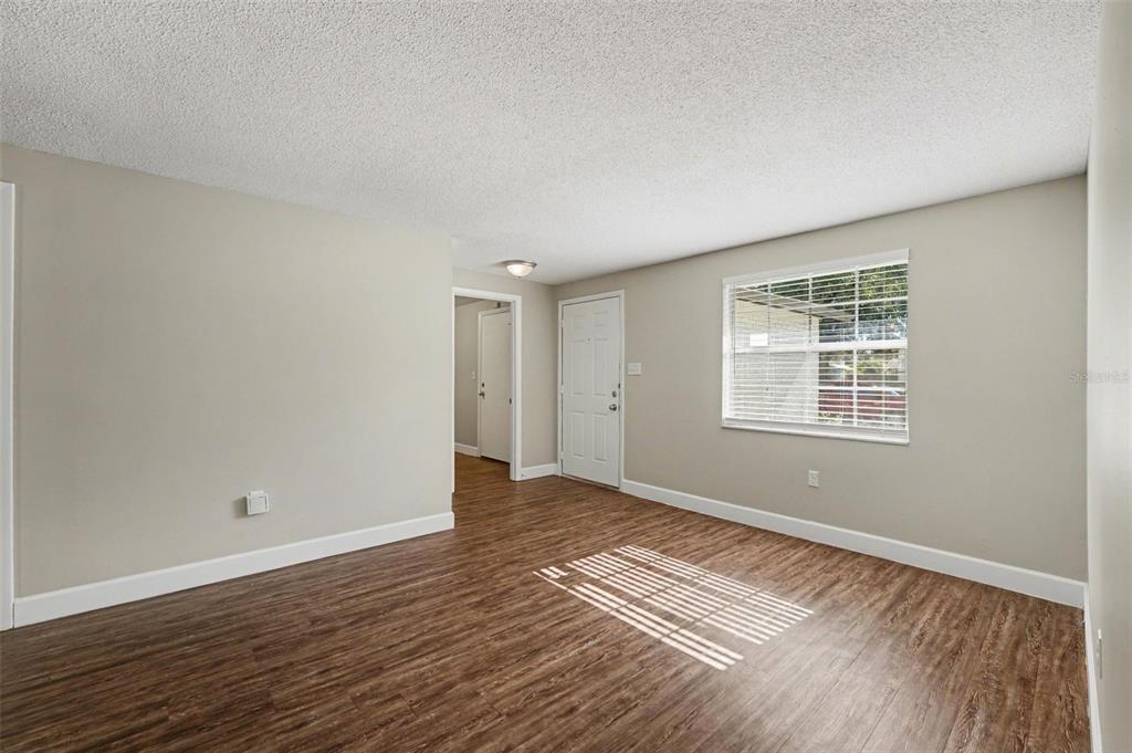 An empty room with wood-look flooring, beige walls, a white door, and a window — 1615 SENECA AVENUE, LAKELAND, FL