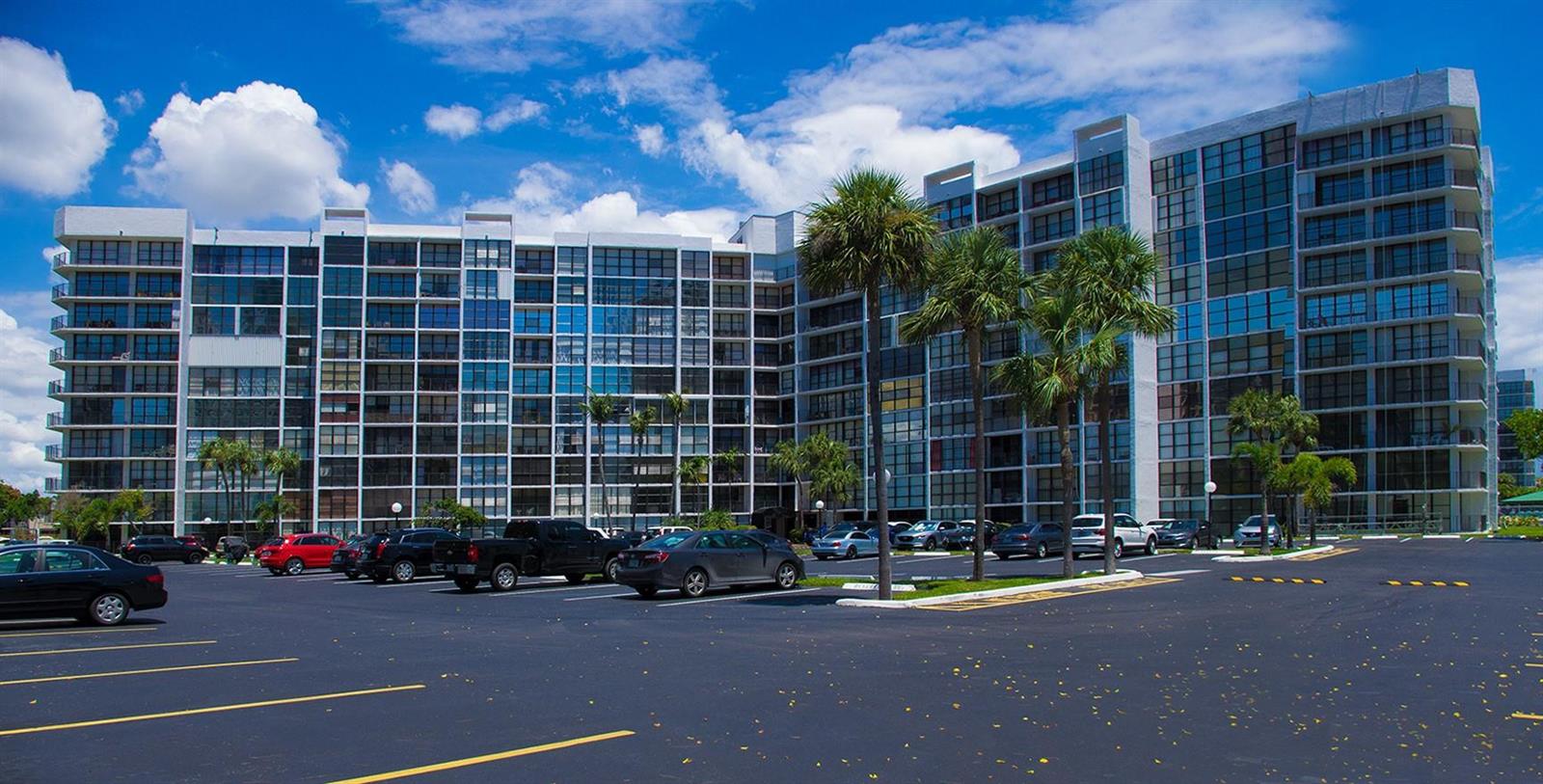 A multi-story apartment building with a large parking lot in the foreground under a blue sky — 800 Parkview Drive # 411, Hallandale Beach FL 33009, HALLANDALE BEACH, FL